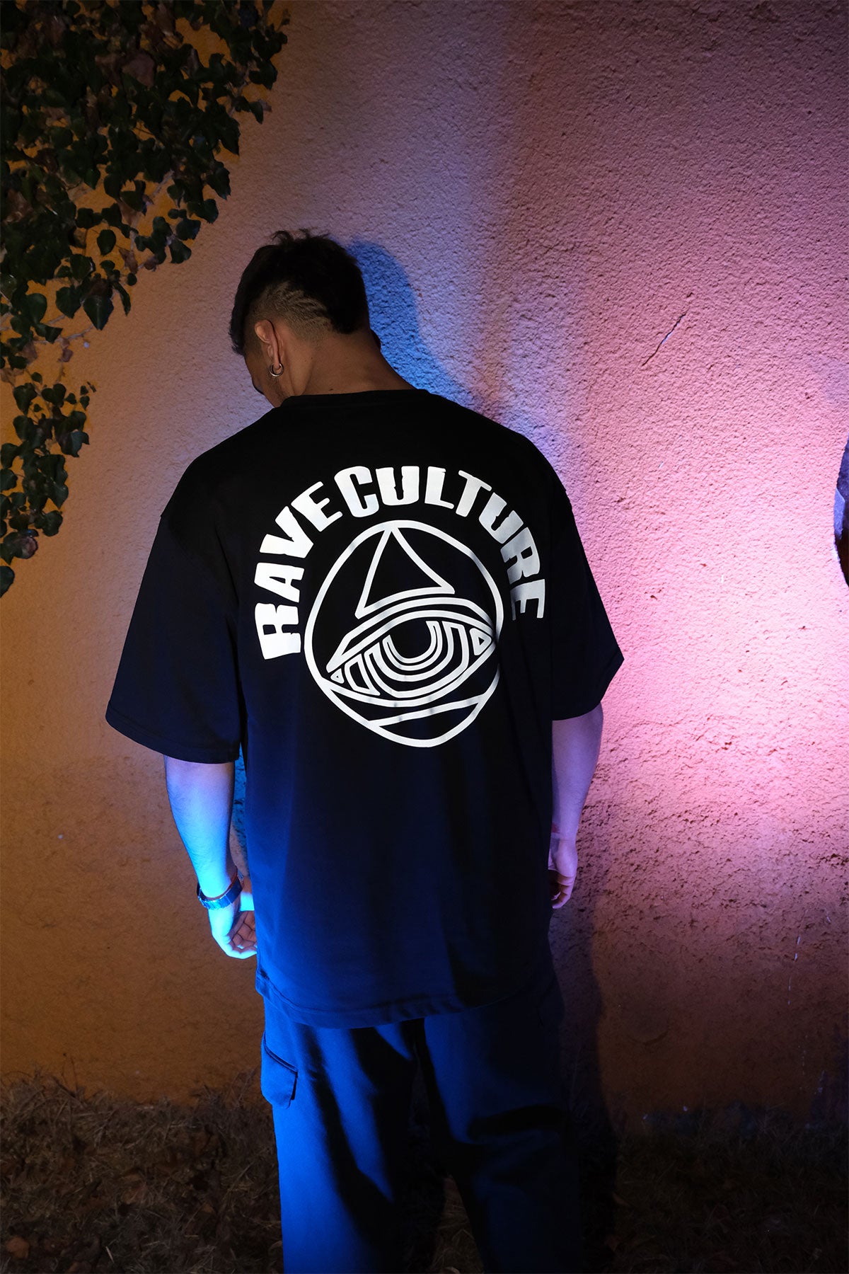 Siyah oversize tişört, arkasında “Rave Culture” yazısı ile, renkli ışıklarla çekilmiş yaratıcı bir görsel.