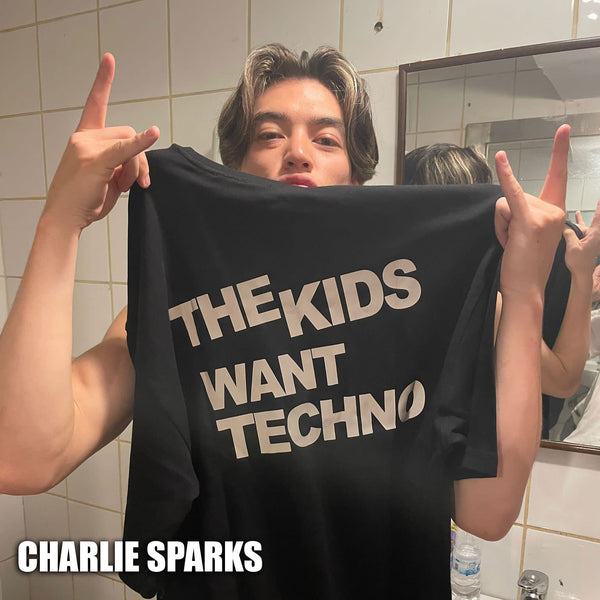 Charlie Sparks is holding an Afterweare T-shirt. The T-shirt features a reflective print and has 'The Kids Want Techno' written on it